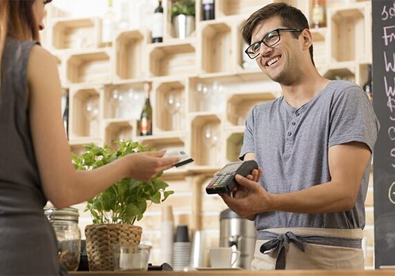 Shot of a smiling barista holding a payment terminal and a customer paying by card